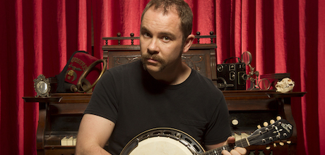 Picture of Producer's Toolbox composer Silas Hite sitting in front of a piano holding a banjo.