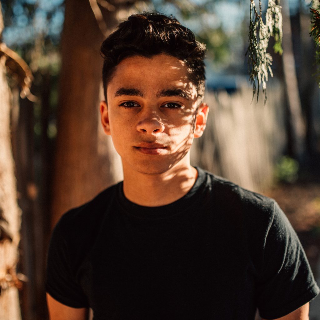 Portrait of Producer's Toolbox composer, Marvin Cruz, standing in front of some trees in a black t-shirt.