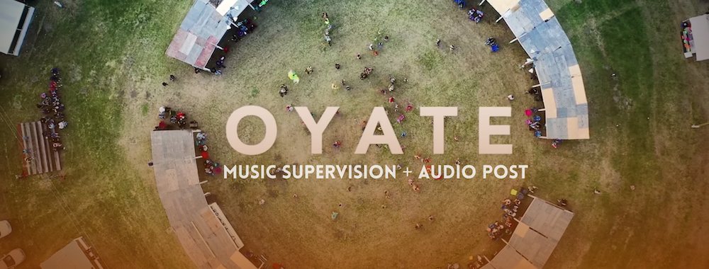 Overhead shot from documentary film, Oyate, of a field with two, large curved lines of pavilions with patchwork roofs nearly meeting to create a large circle. Many people stand under both awnings to watch a round dance taking place in the middle on the grass. Indigenous people of various tribes are dancing in modern and traditional clothes. Overlaid in the center is the name of the film, Oyate, with the words "Music Supervision + Audio Post" below it, and a slight orange gradient overlaying the bottom half of the picture. Flavorlab Sound provided sound design and mix for the film and Producer's Toolbox provided music supervision and clearance for the film.